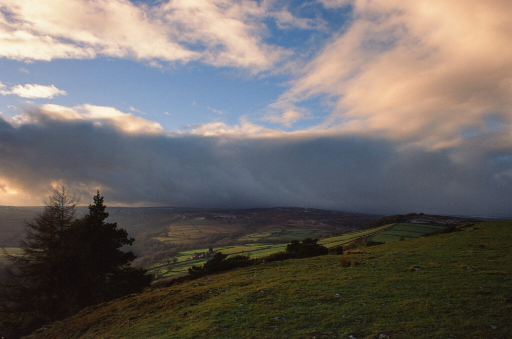 Dark clouds roll in over the green land still catching the afternoon sun.