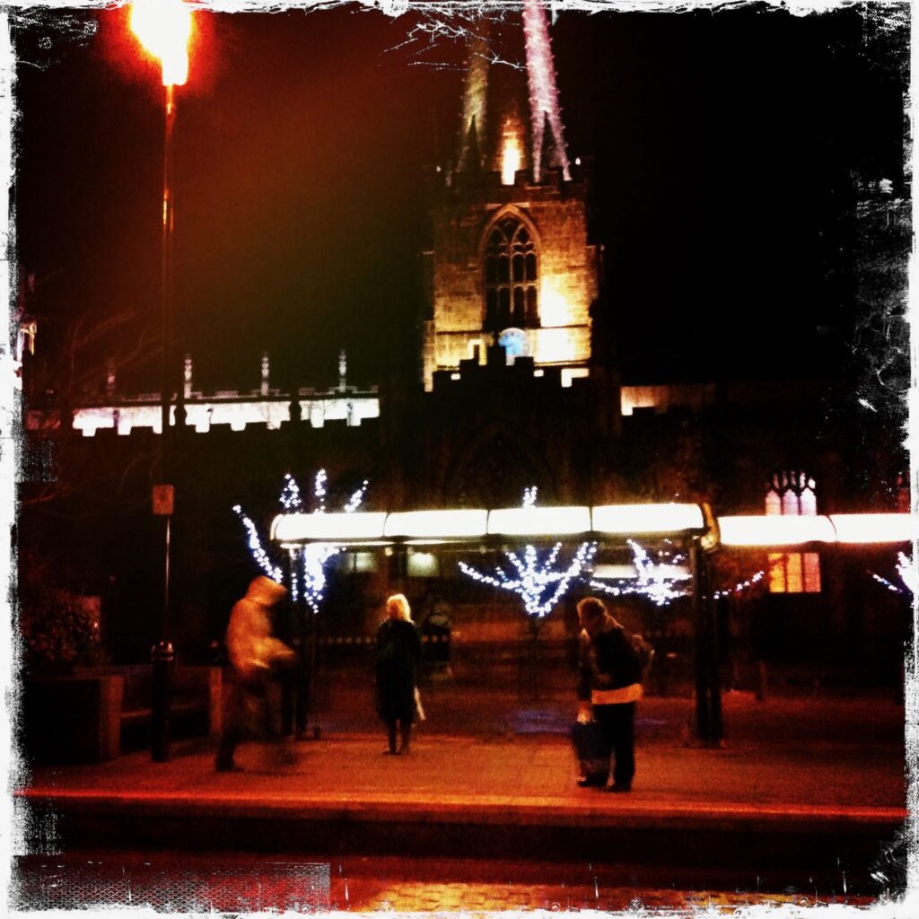 People waiting for a tram under the lights of Sheffield Cathedral.