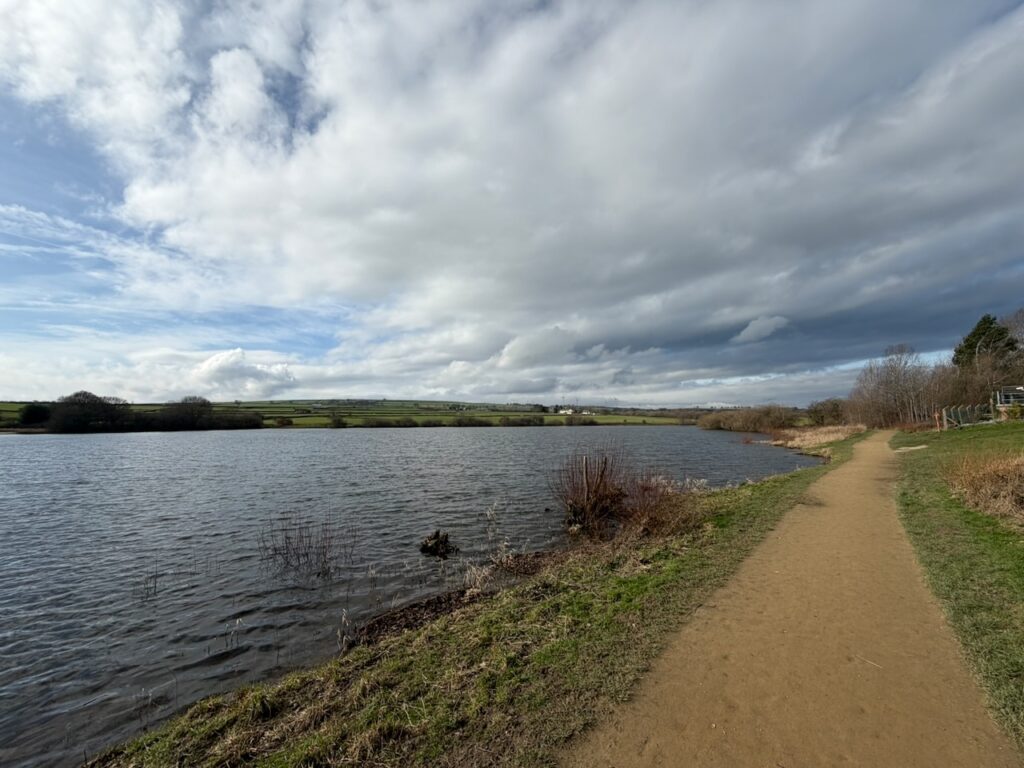 A path by a reservoir under an overcast sky.